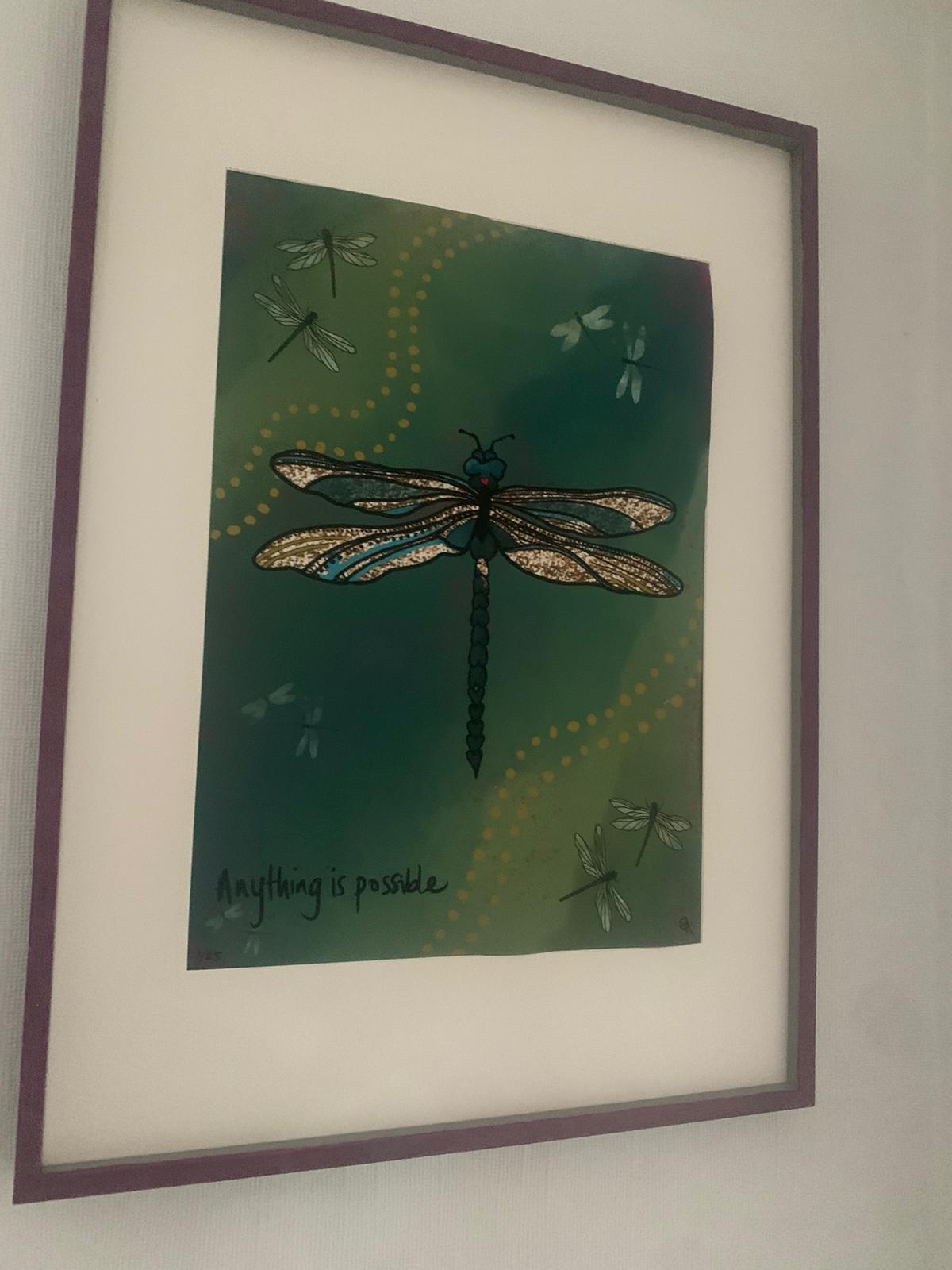 Framed artwork with a dragonfly design and motivational quote on a green background.