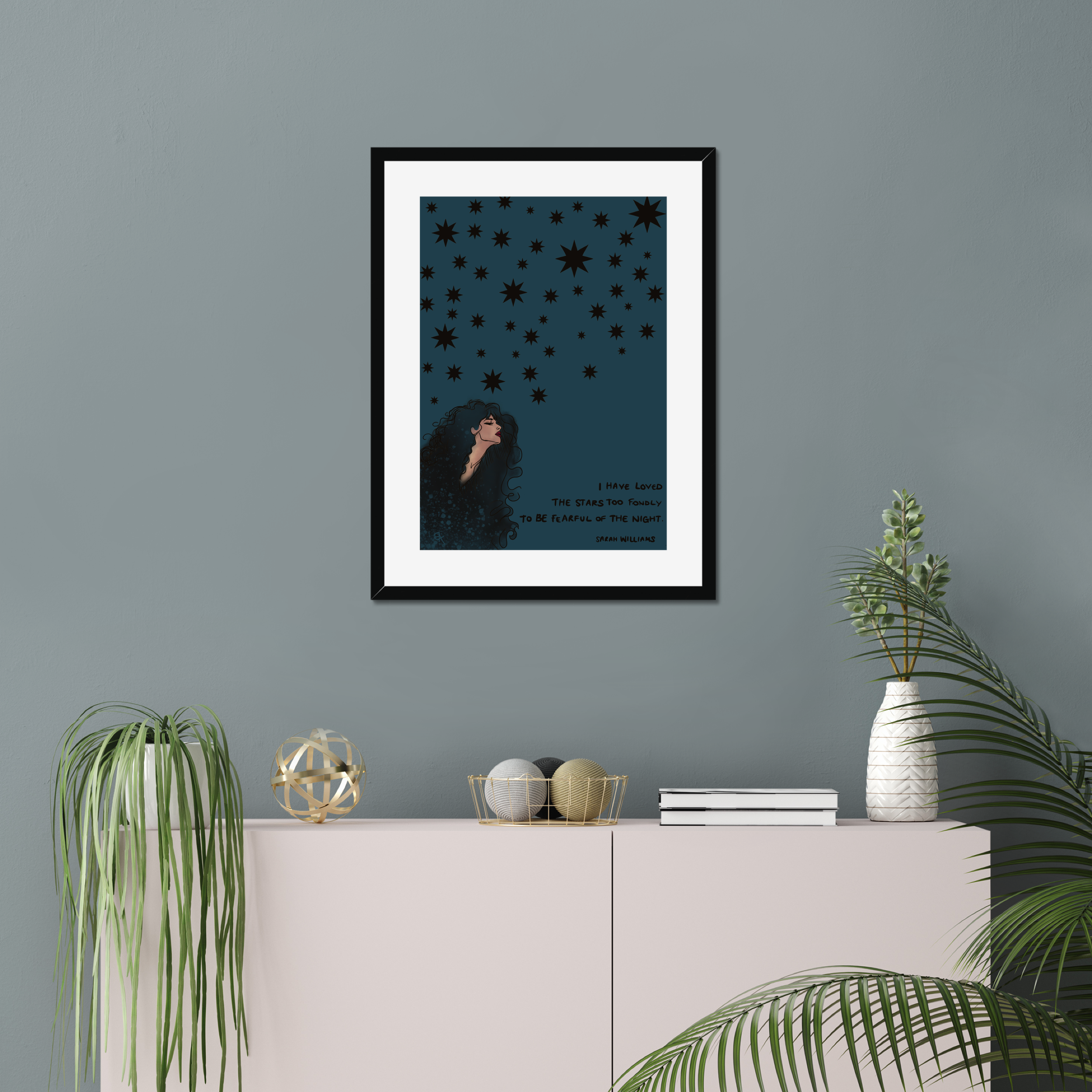 Framed artwork of a woman gazing at stars on a gray wall above a white cabinet with decorative items.